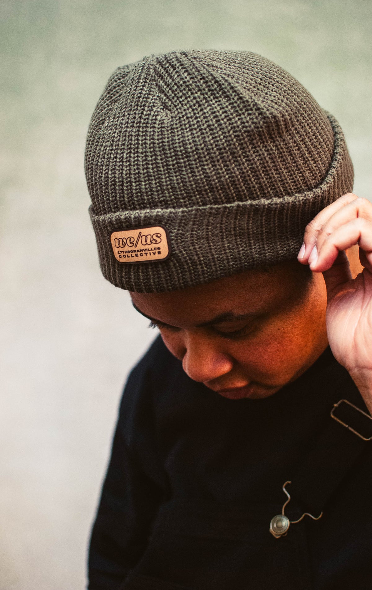 Person wearing a brown knit beanie with a leather patch on a neutral background