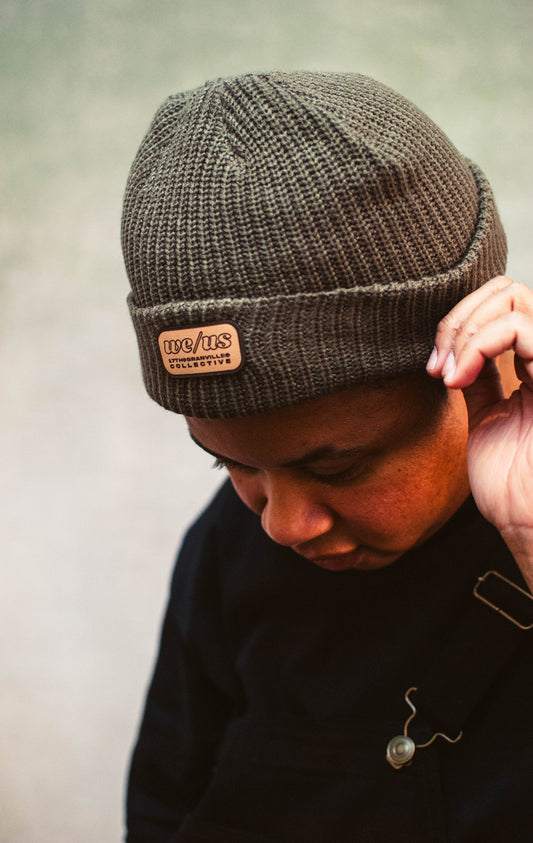 Person wearing a brown knit beanie with a leather patch on a neutral background