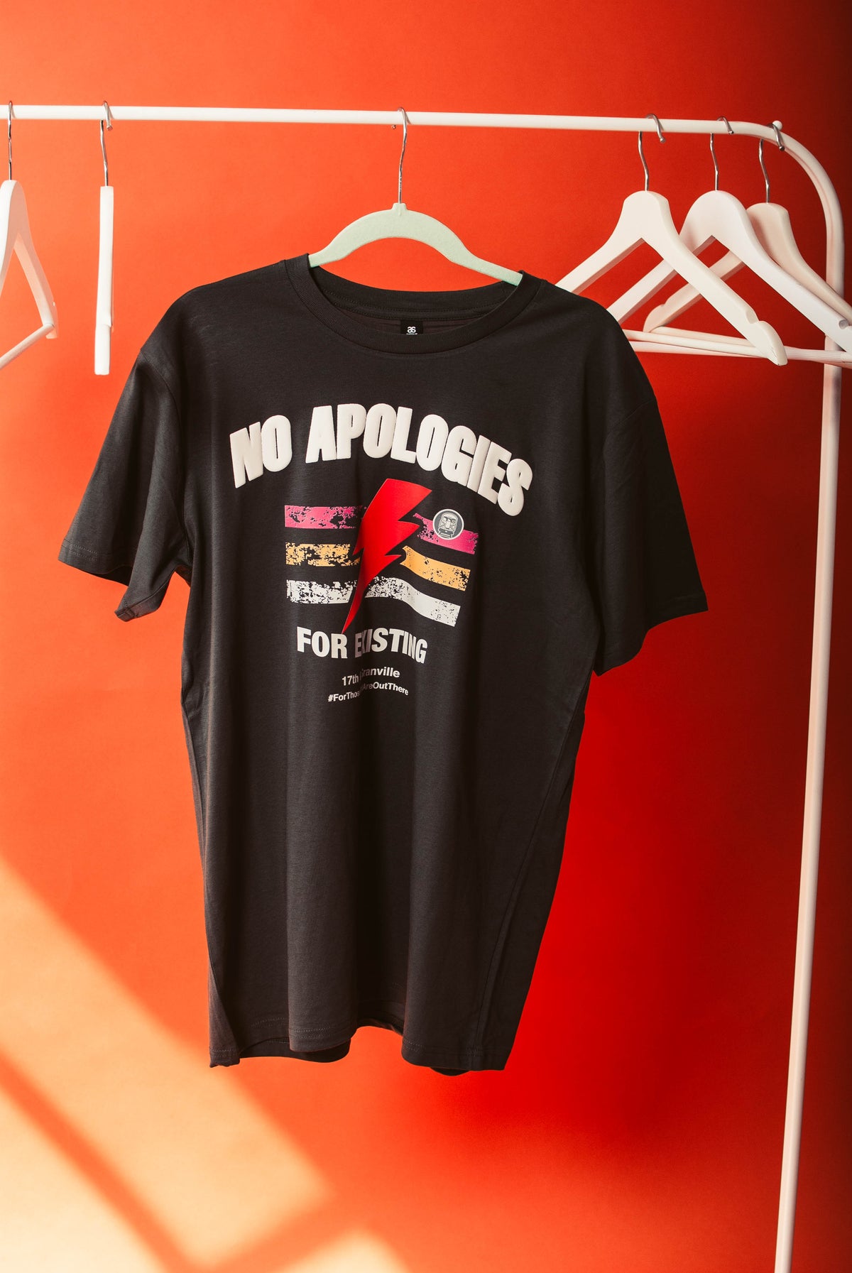 17th & Granville t-shirt with 'No Apologies' text and graphic on a hanger against an orange wall.