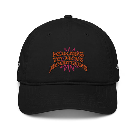 A stylish black hat crafted from organic cotton, adorned with vibrant orange and pink embroidery on the front showcasing "LEARNING TO MOVE MOUNTAINS," along with 17th & Granville's discreet logo on the right side.