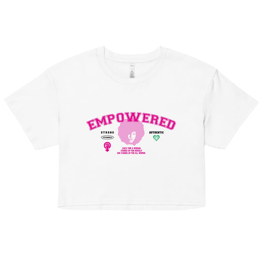 The Empowered Crop Top by 17th & Granville showcases pink EMPOWERED lettering on a white background. Beneath it, there's a stylized female symbol with a raised fist, accompanied by the words STRONG and ATHLETIC. Made from premium fabric by this black-owned brand, the top features extra symbols to amplify its striking design.