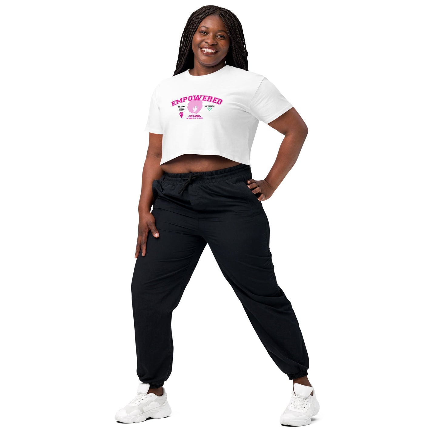 A person stands confidently with a smile, wearing the Empowered Crop Top crafted from high-quality fabric paired with black joggers from 17th & Granville. Their long braided hair frames their face as they pose against a plain white background, proudly showcasing apparel from this black-owned company.