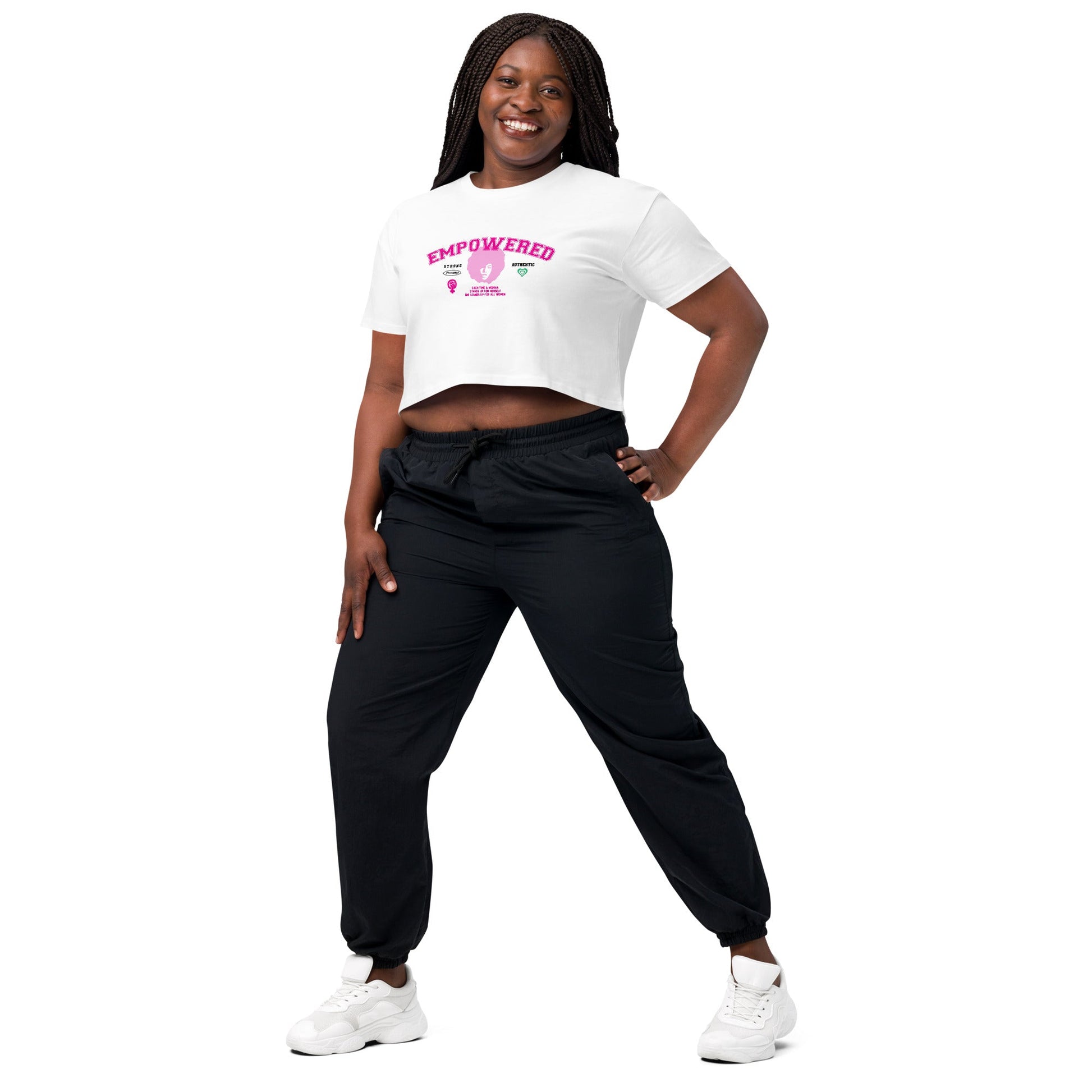 A person stands confidently with a smile, wearing the Empowered Crop Top crafted from high-quality fabric paired with black joggers from 17th & Granville. Their long braided hair frames their face as they pose against a plain white background, proudly showcasing apparel from this black-owned company.