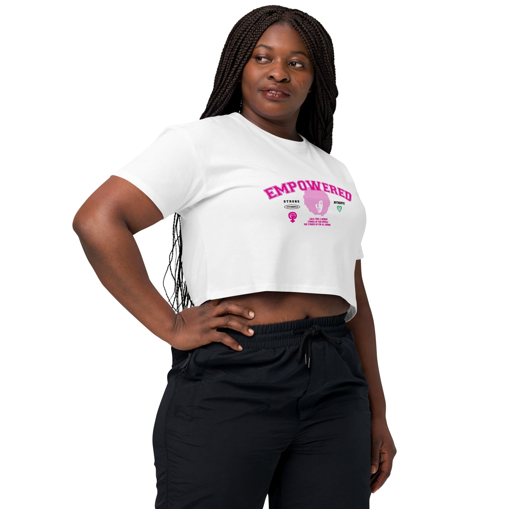 A woman with long braided hair confidently models an Empowered Crop Top crafted from premium fabric, paired with black pants. With one hand on her hip against a plain white background, she embodies the spirit of the black-owned brand 17th & Granville.