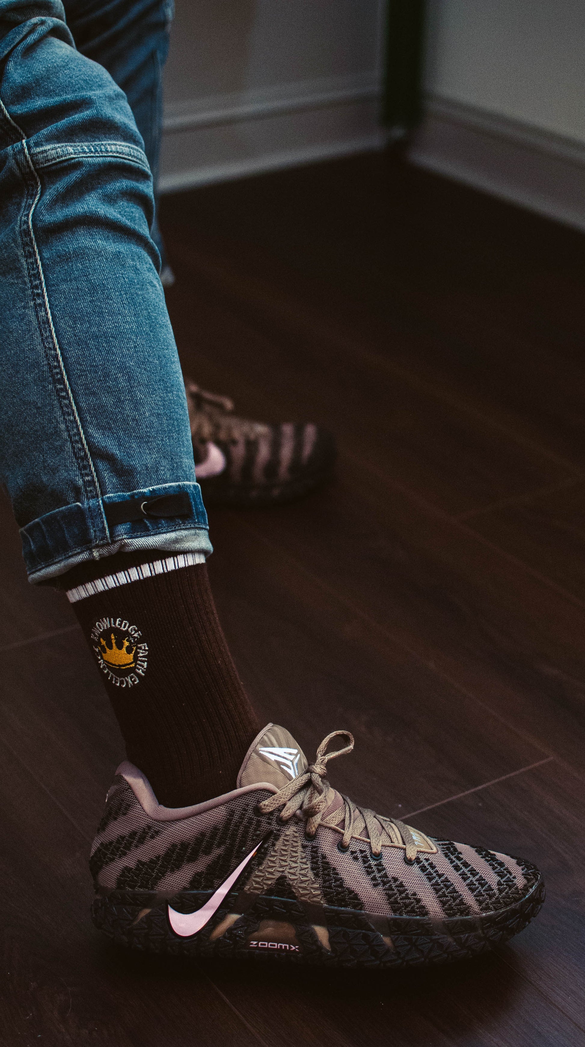 Person wearing 17th and Granville Black Excellence sock with a logo and a sneaker on a wooden floor.