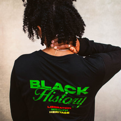 Person wearing a black long-sleeve shirt with 'Black History' text in green and yellow on the back, against a textured gray background.