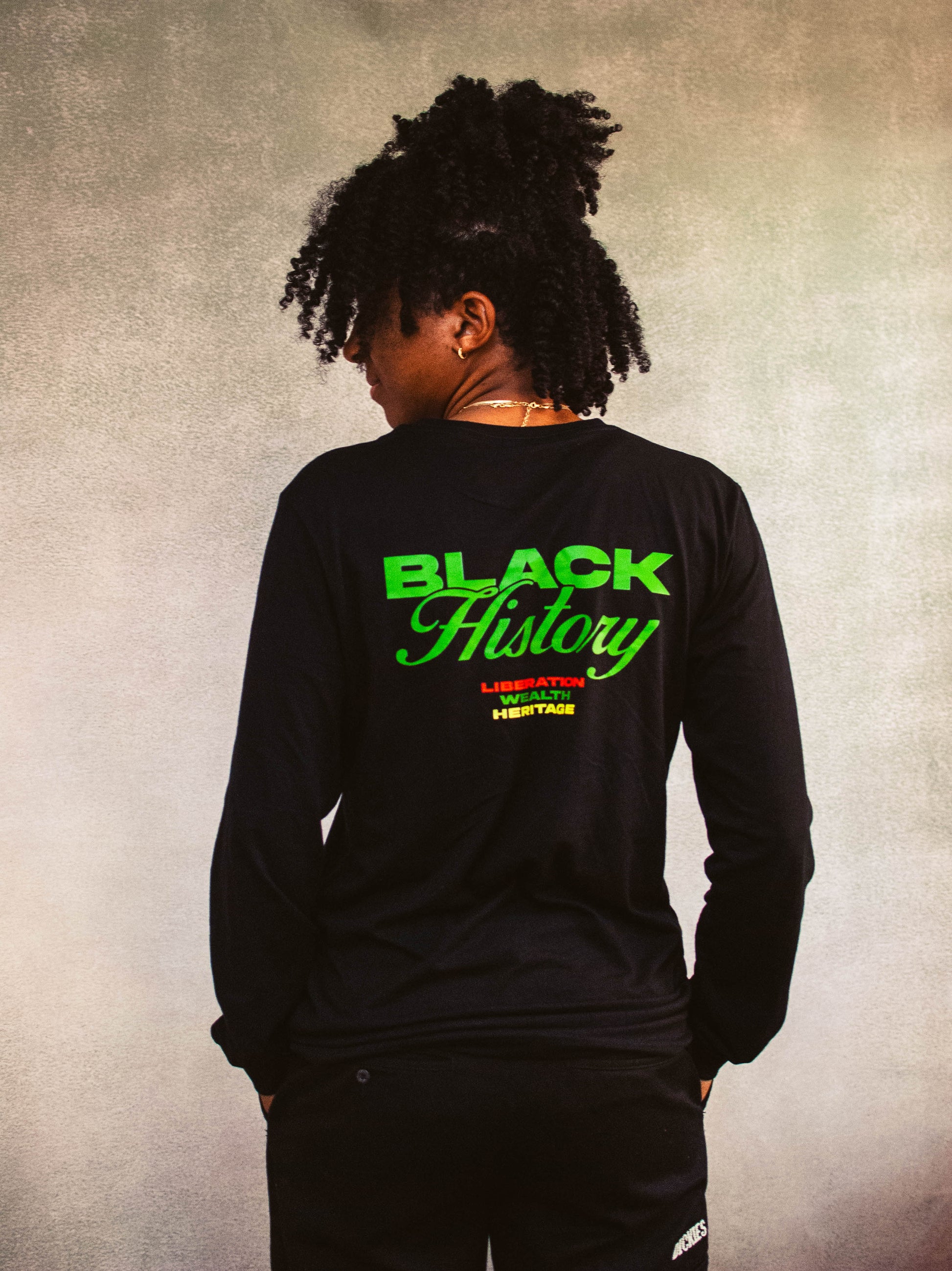 Person wearing a black long-sleeve shirt with 'Black History' text on the back against a textured beige background
