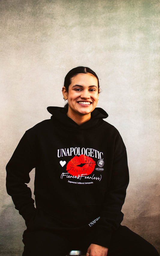 Person wearing a black hoodie with a graphic design centered on being unapologetic, fierce, and fearless on a textured gray background