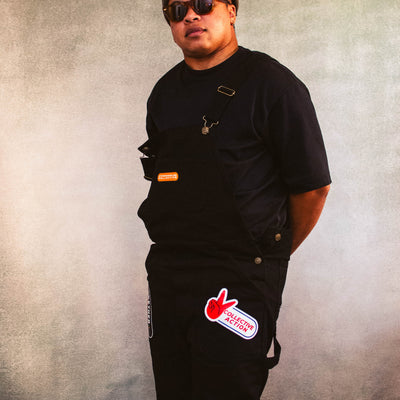 Person wearing 17th and Granville black overalls with a collective action logo on pants against a textured gray background