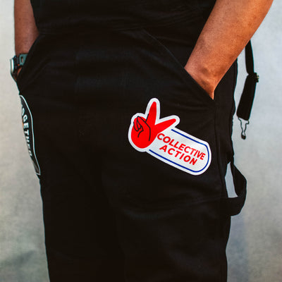 Black overalls with a collective action patch on a plain background