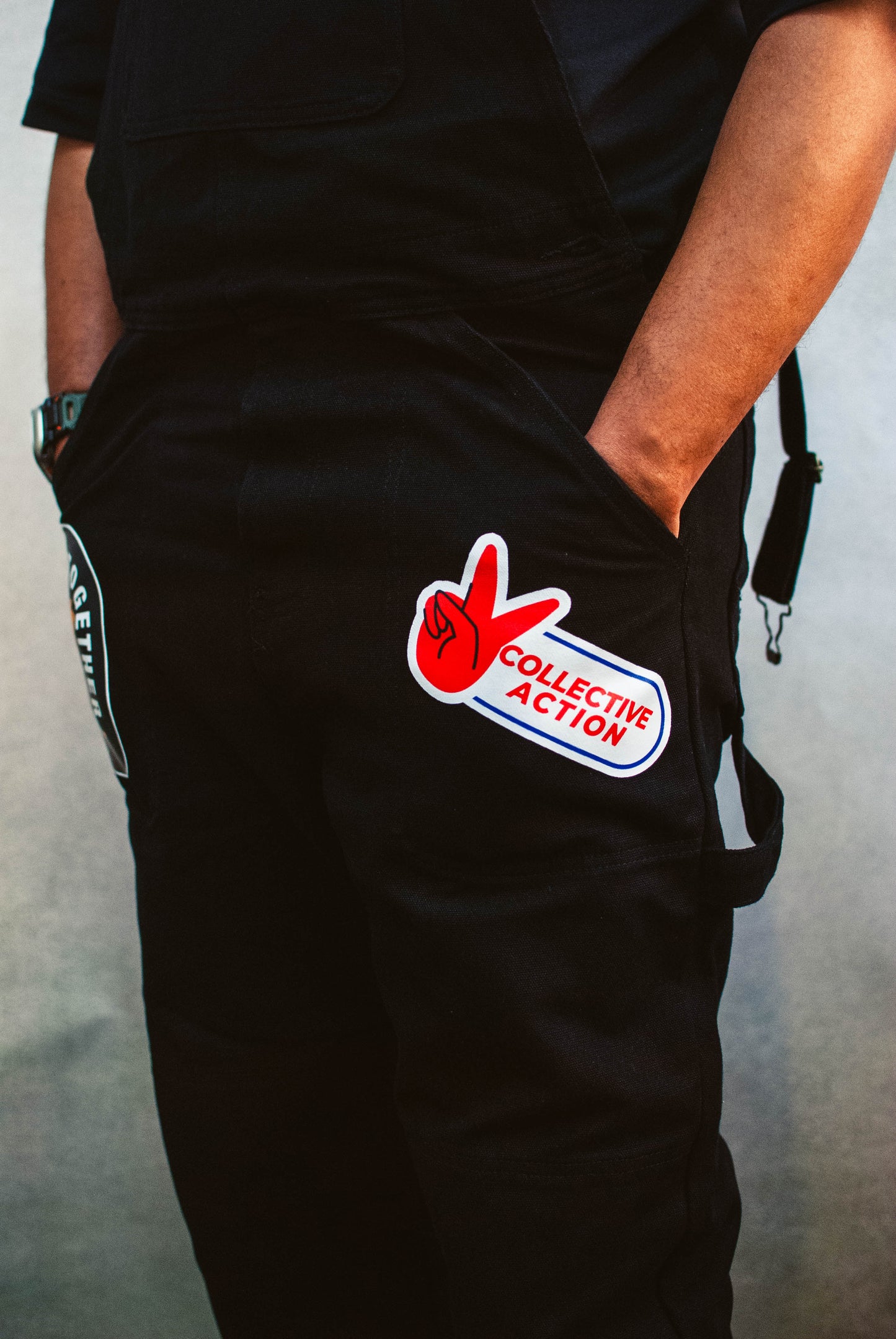 Black overalls with a collective action patch on a plain background