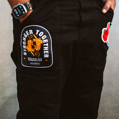 Black overalls with a 'Stronger Together' patch on a gray background