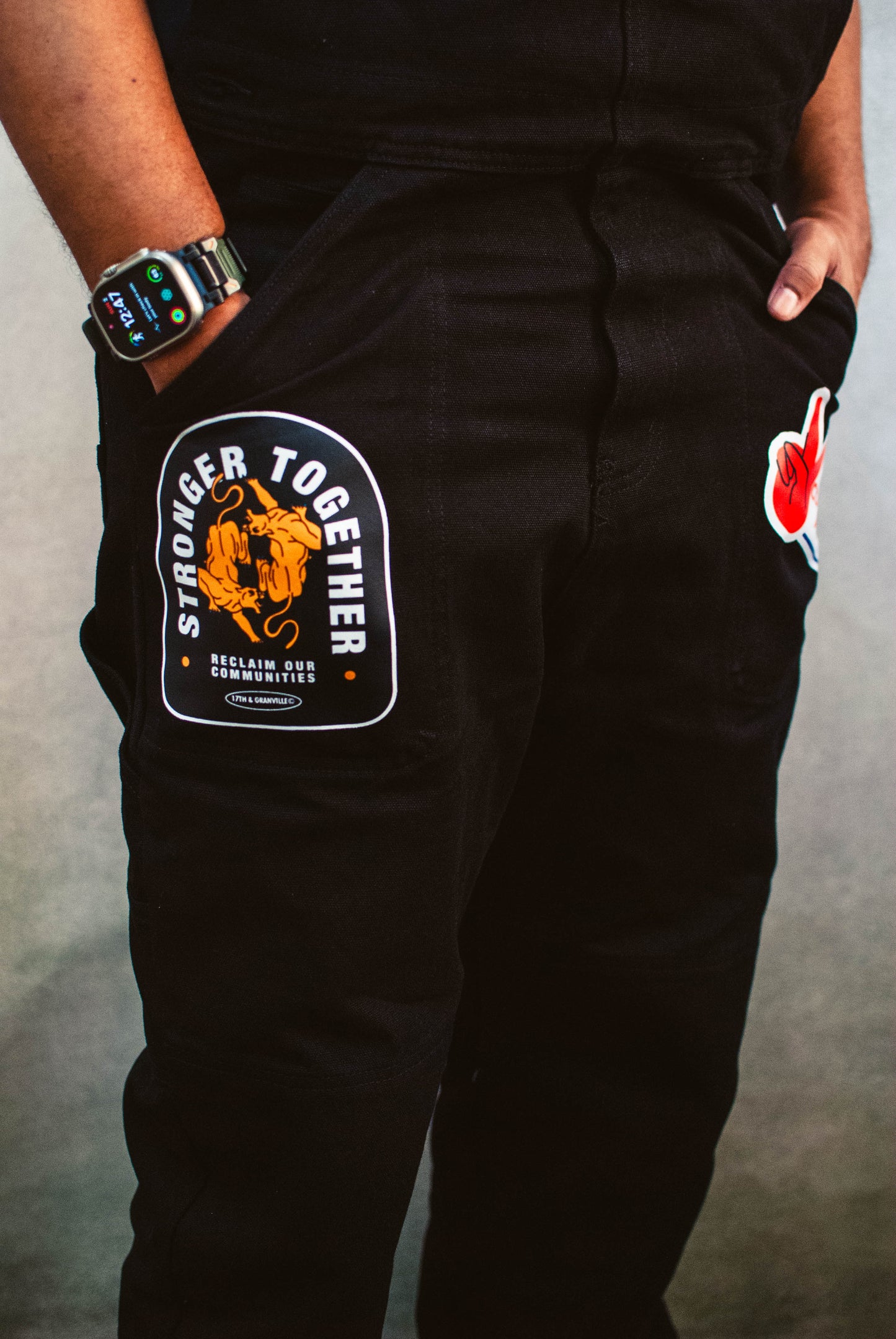 Black overalls with a 'Stronger Together' patch on a gray background