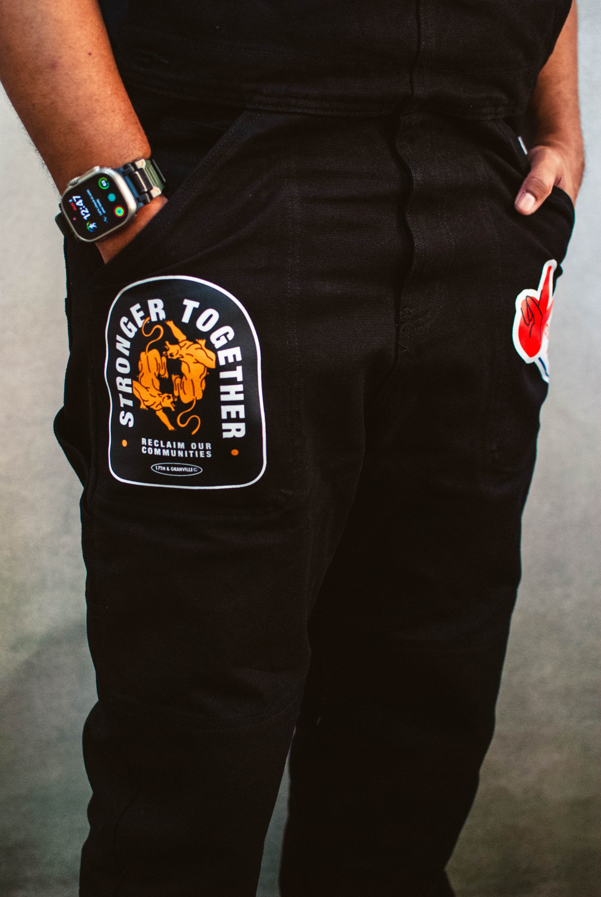 Black overalls with a 'Stronger Together' patch on a gray background