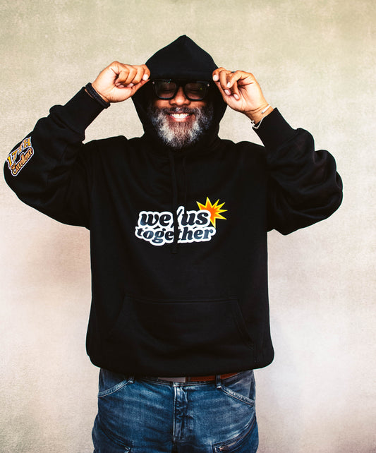 Person wearing a black hoodie with 'we/us together' text on a textured wall background