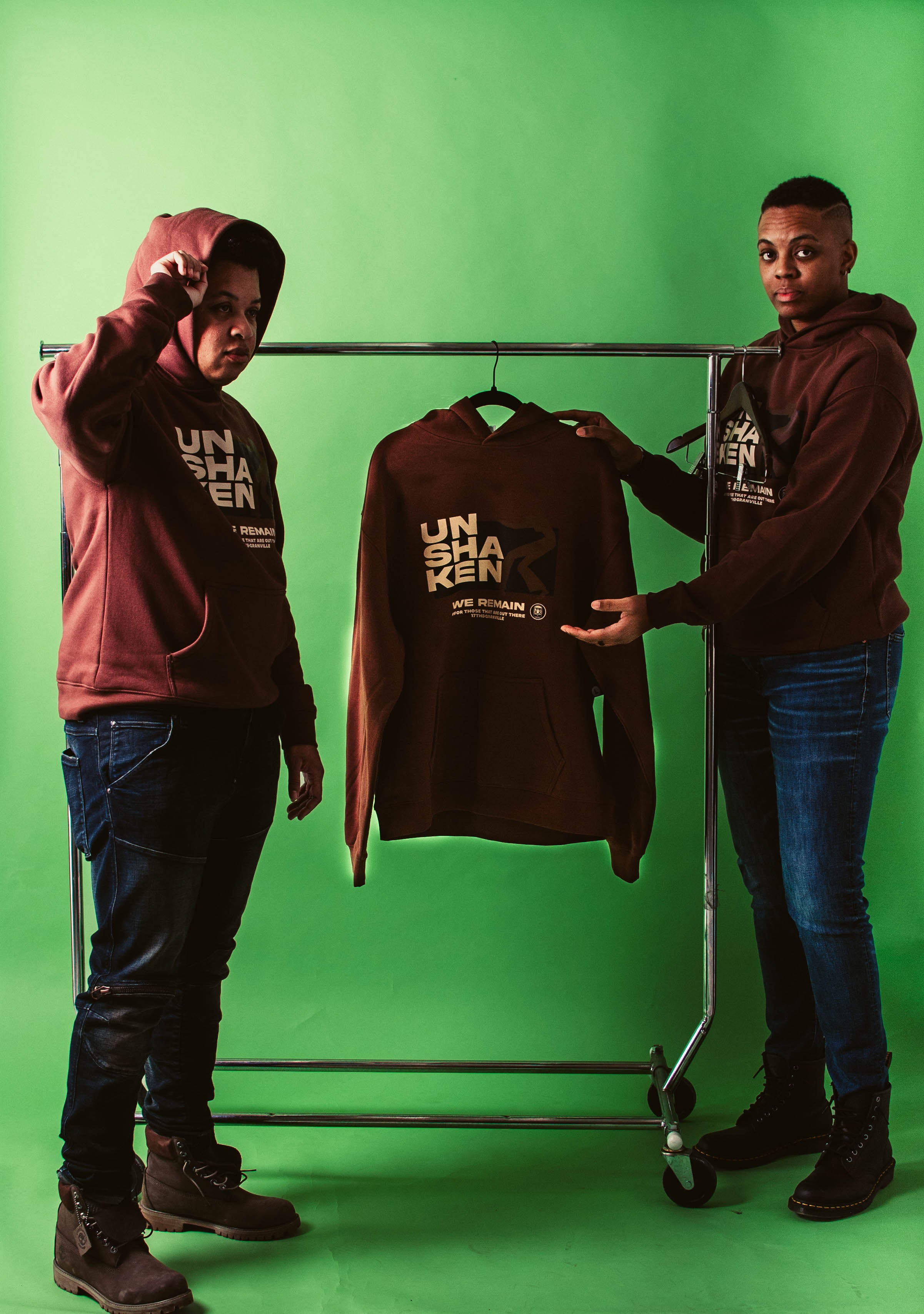 Two people standing next to a rack with a brown hoodie on a green background