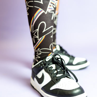 Close up of Blooming Pride socks paired with black and white sneakers.
