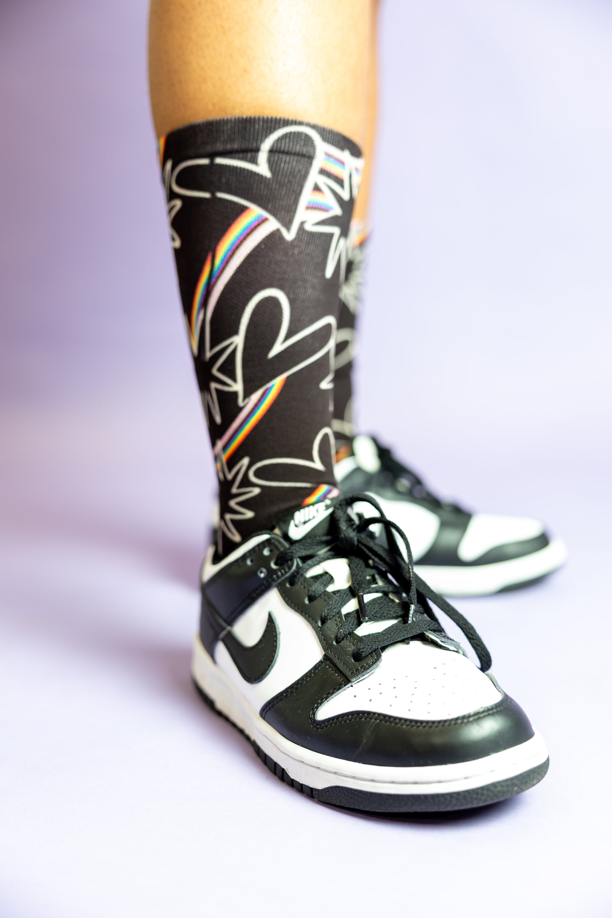 Close up of Blooming Pride socks paired with black and white sneakers.