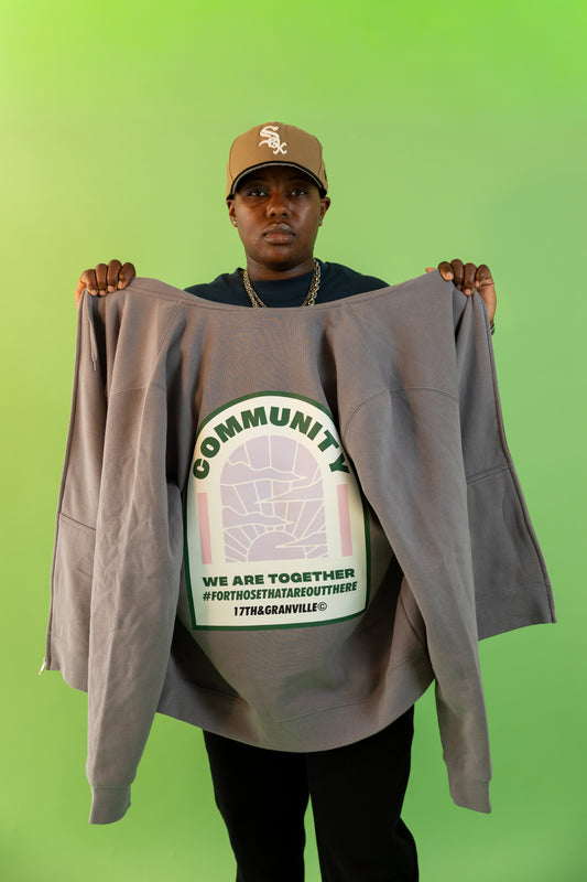 Person holding a Community Together Hoodie by 17th & Granville – zip-up fleece with bold We Are Together back graphic and chest print