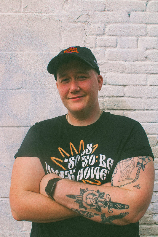 Black organic cotton hat and t-shirt from the Eintou Collection by 17th & Granville, featuring embroidered design with poetry snippets, part of a fashion activism collaboration supporting BIPOC and LGBTQ+ communities.