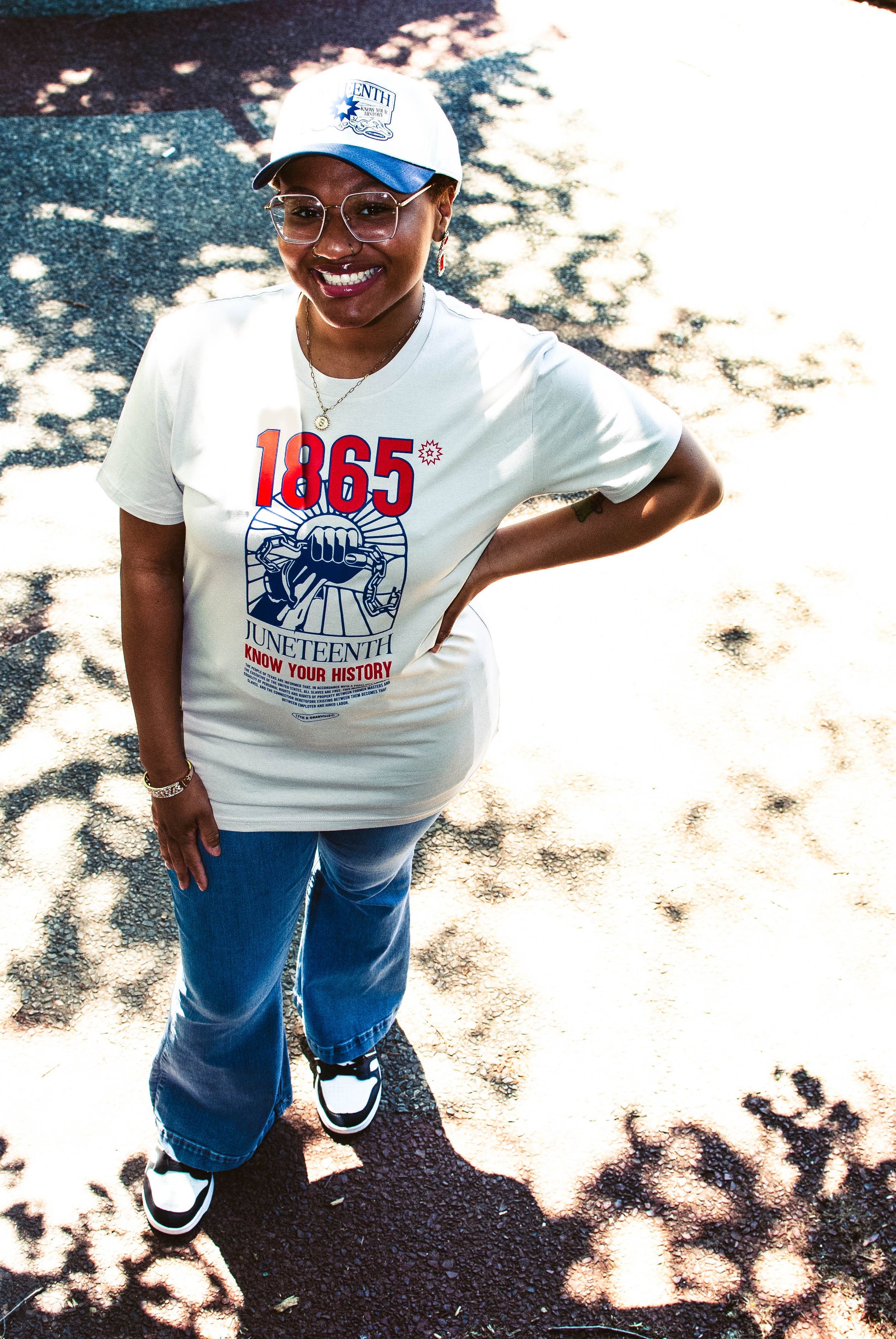 Model wearing Juneteenth 'Know Your History' tee in bone, standing face forward to display front graphic with raised fist and 1865 design