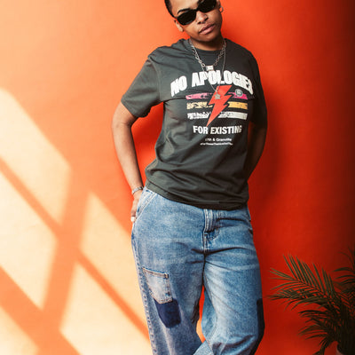 Person wearing a No Apologies t-shirt and jeans against an orange wall