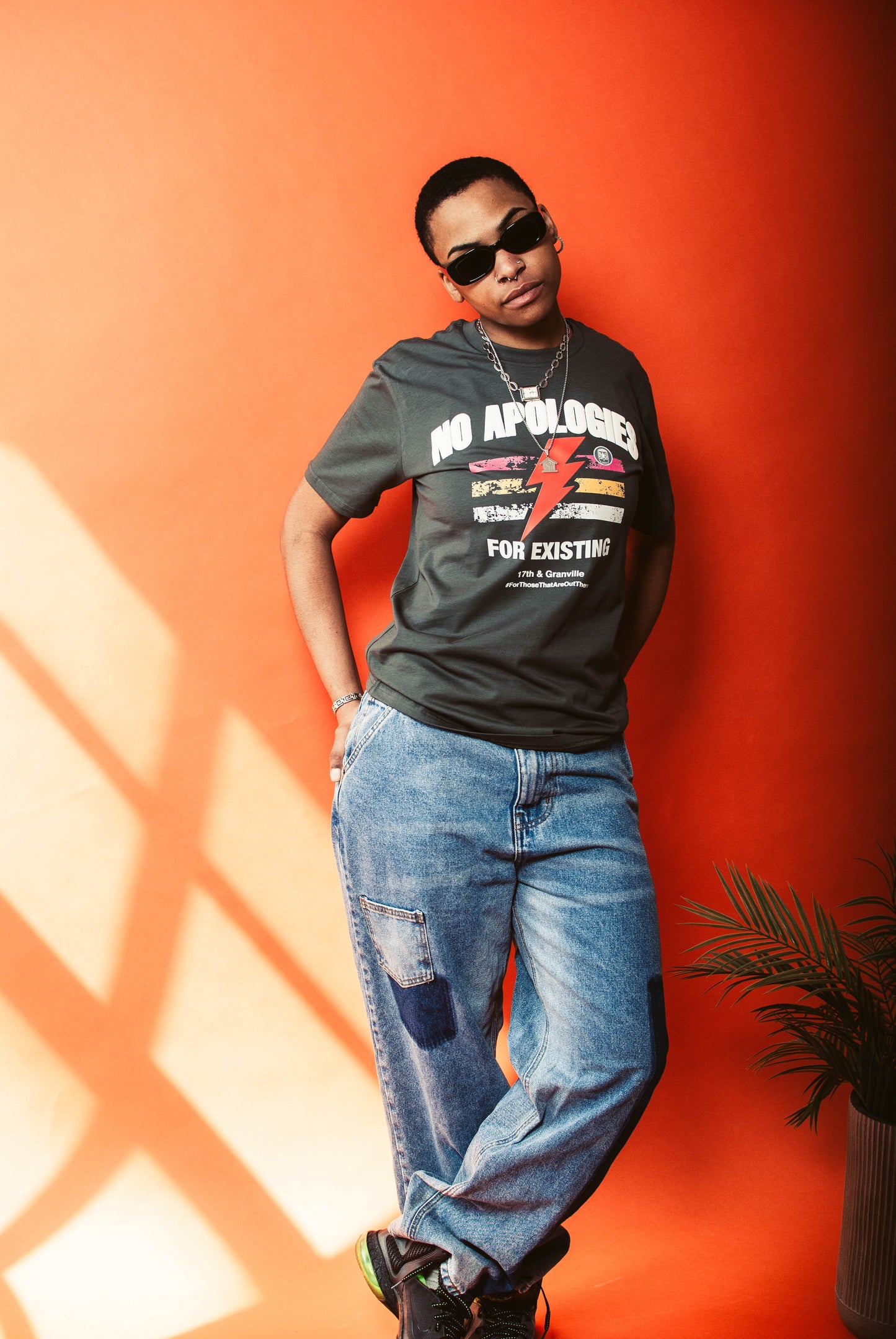 Person wearing a No Apologies t-shirt and jeans against an orange wall