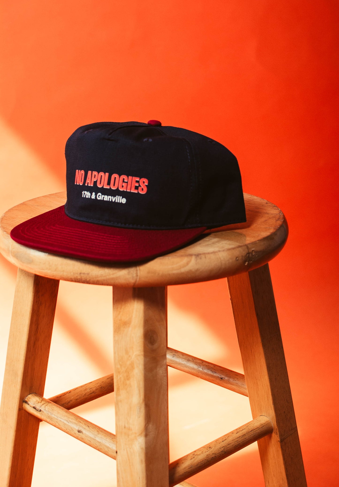 17th & Granville No Apologies Hat on a wooden stool with orange background 