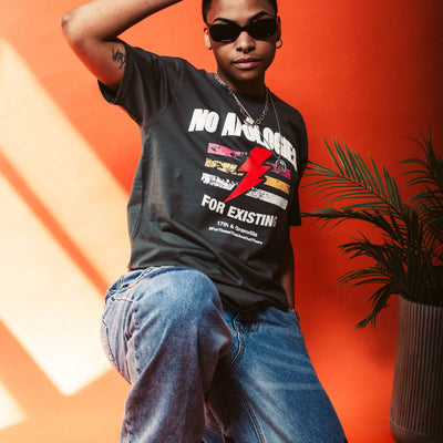 Person wearing a No Apologies t-shirt from 17th & Granville with graphic design and text, sitting on an orange background.