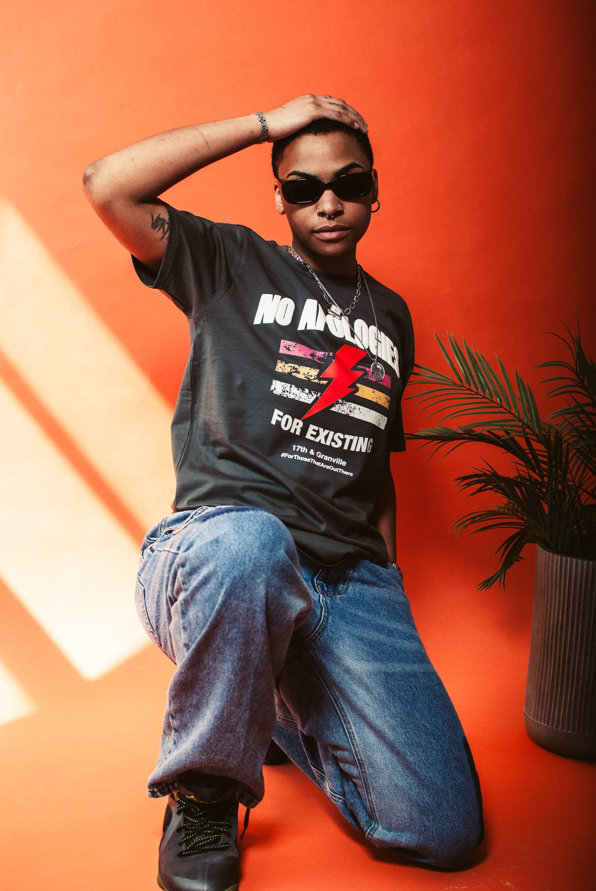 Person wearing a No Apologies t-shirt from 17th & Granville with graphic design and text, sitting on an orange background.