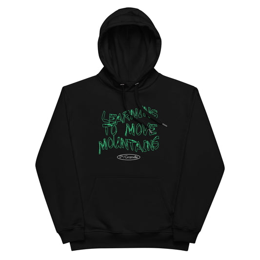 A black poetry hoodie from 17th & Granville showcases green graffiti-style text that says "Learning to Move Mountains." Beneath this message is a small oval with the word "Organic," emphasizing its creation from organic cotton.